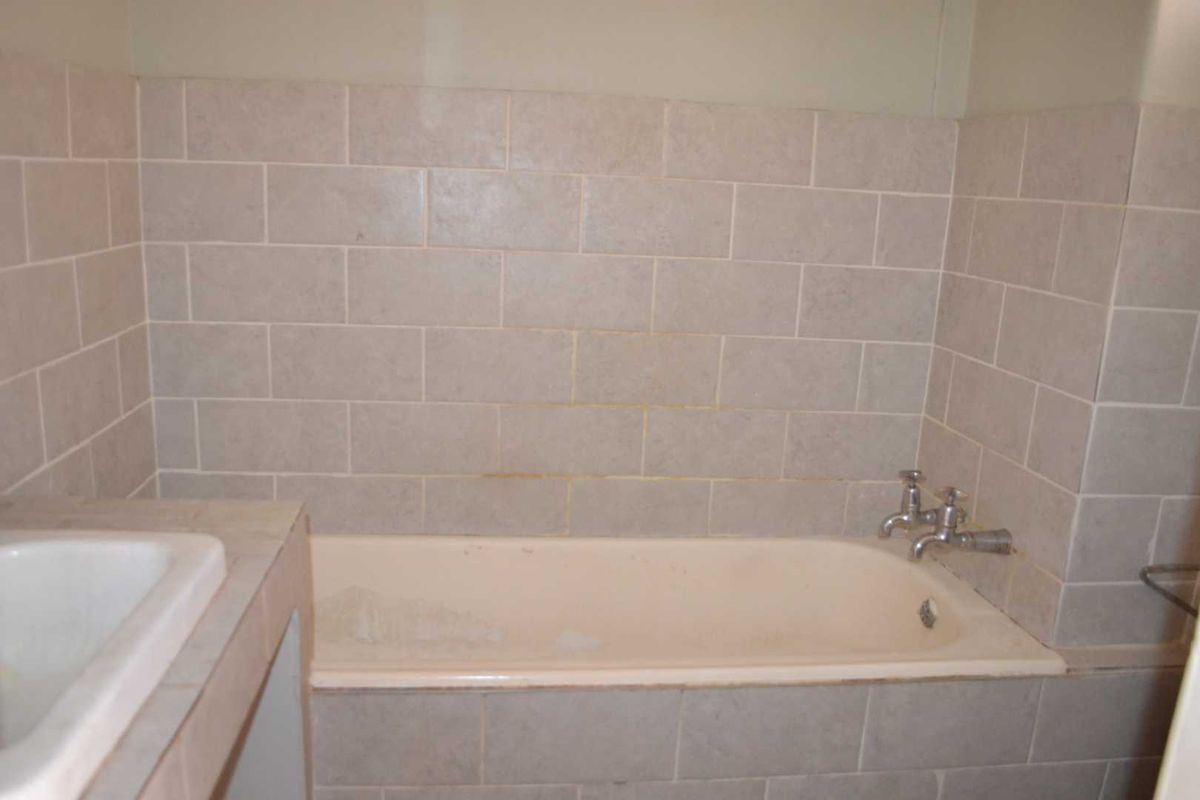 A dated bathroom featuring a built-in bathtub with tiled surround and a vanity basin, requiring cosmetic updates to improve its overall condition.