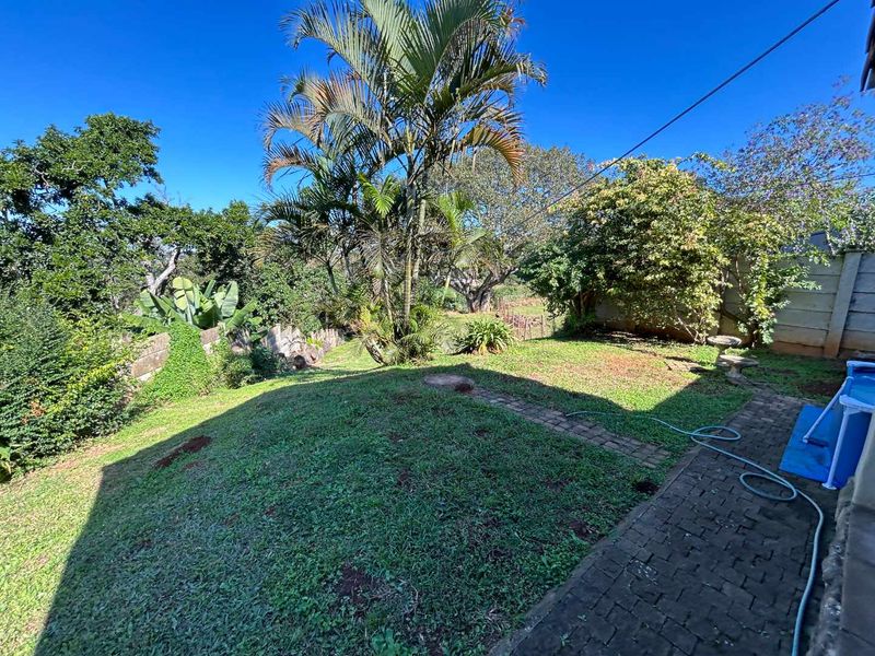 A spacious rear garden featuring a paved walkway, established trees, and a boundary wall, offering a private outdoor space.