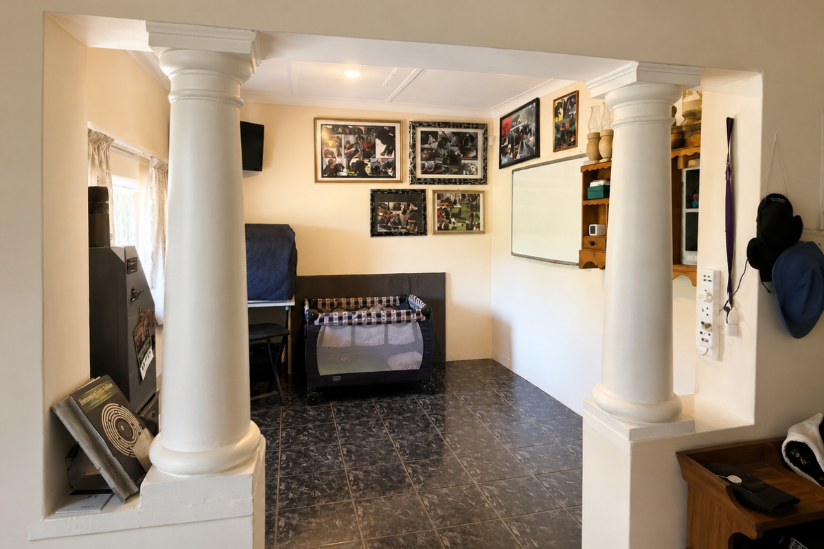 A living area featuring decorative columns, tiled flooring, and built-in wall shelving, offering a versatile space for various uses.