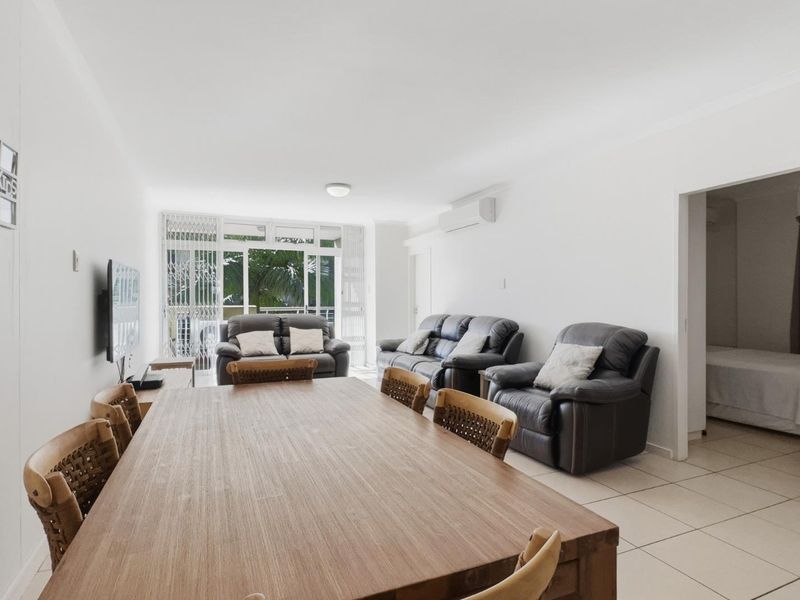 Spacious open-plan living and dining area featuring neutral tiled flooring, split-system air conditioning, and direct access to a balcony through sliding glass doors.