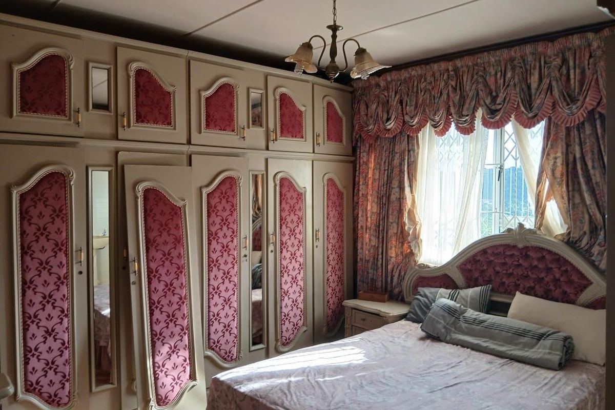 A bedroom featuring extensive built-in cabinetry with decorative paneling and a window fitted with a security gate.