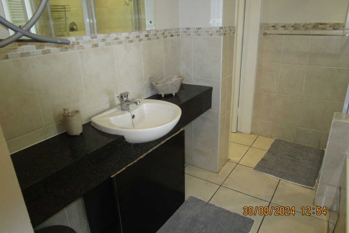 A functional bathroom featuring a granite-topped vanity with a ceramic basin, tiled walls, and a shower enclosure.