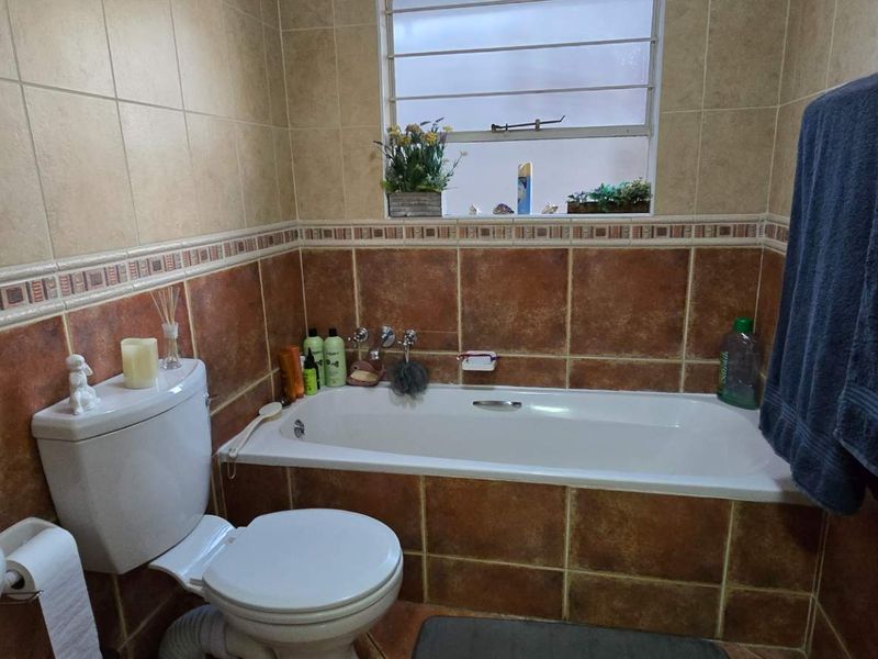 A functional bathroom featuring a bathtub, toilet, and pedestal basin with warm-toned wall tiling and a louvered window for ventilation.