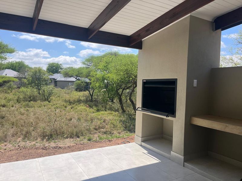 A covered patio featuring a built-in braai, concrete countertop, and tiled flooring, overlooking a natural bushveld landscape.