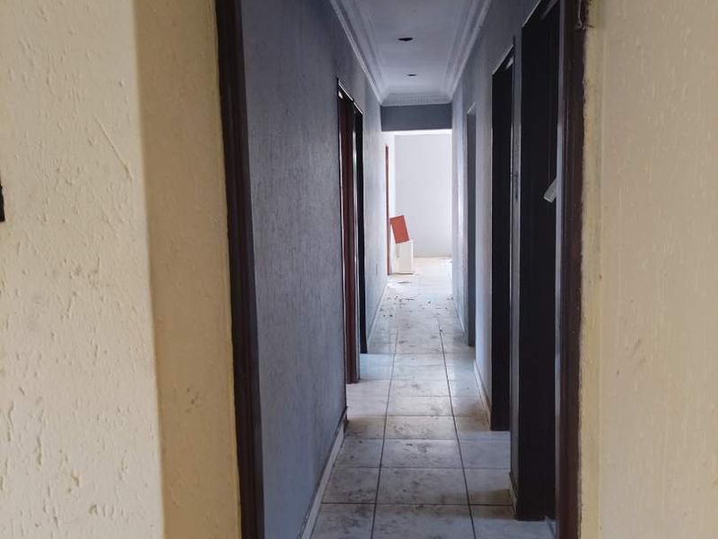 A narrow interior hallway featuring tiled flooring and dark door frames, currently in need of cosmetic refurbishment and repairs to the ceiling and walls.