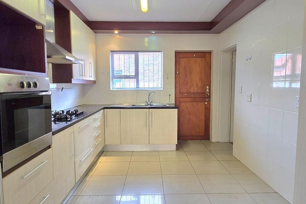 A functional kitchen featuring light-toned cabinetry, dark countertops, a built-in oven, gas hob, and tiled flooring with direct access to an exterior door.