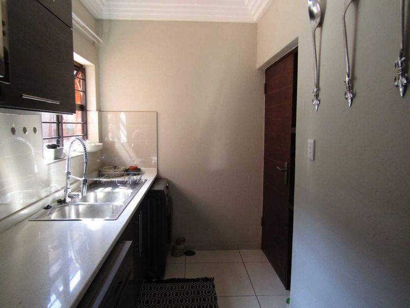 A functional scullery featuring a double basin sink, stone countertops, tiled splashbacks, and built-in cabinetry with direct access to an adjacent room.
