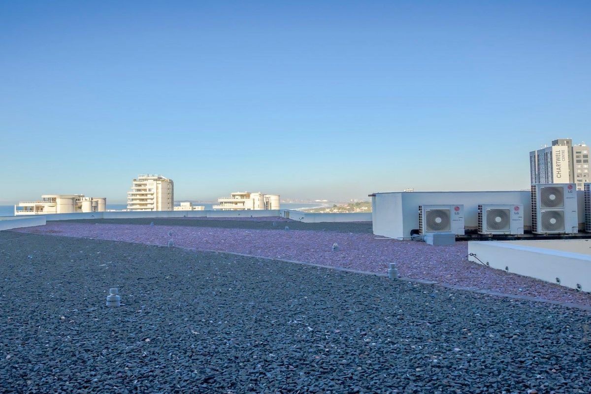 A rooftop area featuring gravel surfacing and multiple air conditioning condenser units, offering expansive views of the surrounding urban landscape and coastline.