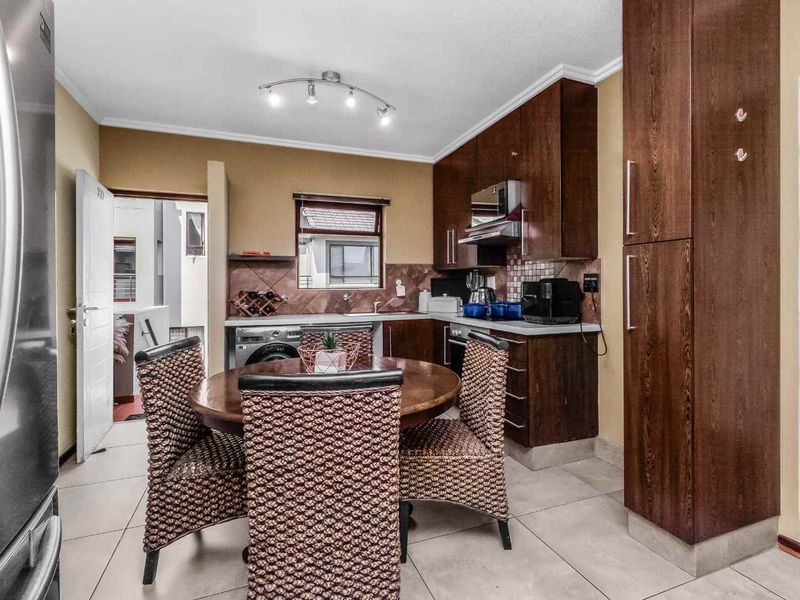 A functional kitchen featuring dark wood cabinetry, built-in appliances, tiled flooring, and a dedicated dining area with a tiled backsplash.