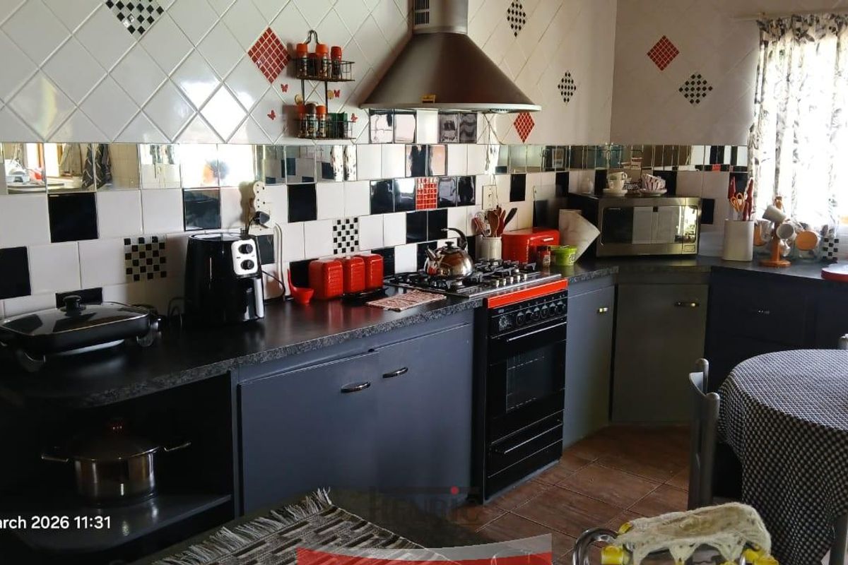 A functional kitchen featuring dark cabinetry, a gas hob with extractor fan, and a distinctive black and white tiled backsplash.