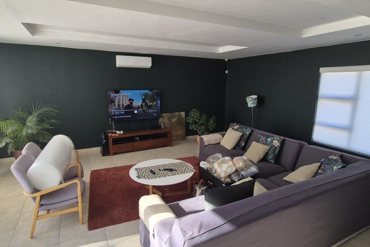 A spacious living room featuring tiled flooring, a recessed ceiling design, and a wall-mounted air conditioning unit.