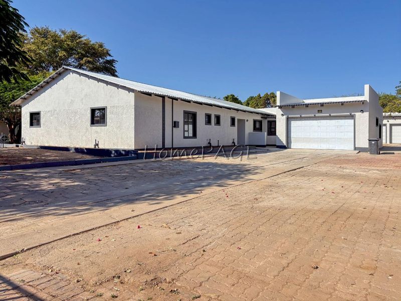 Front exterior view of a single-story house featuring a paved driveway, garage, and textured stucco facade under a metal roof.