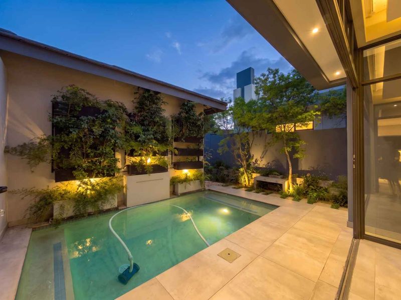 A beautifully illuminated outdoor pool area featuring a vertical garden, modern tiled patio, and seamless transition to the interior through large sliding glass doors.