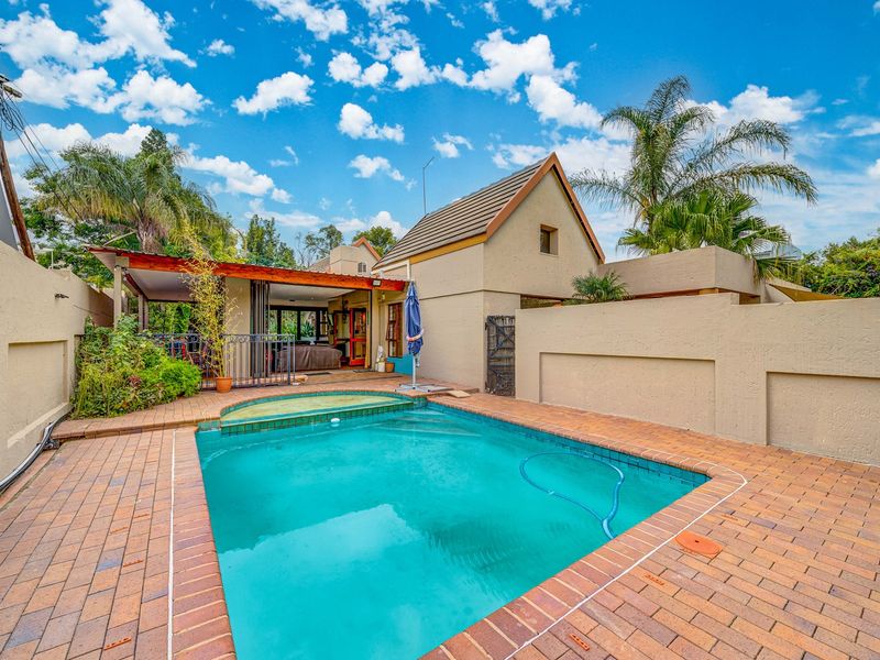 Outdoor pool area featuring a swimming pool with brick paving, a covered patio, and surrounding boundary walls.
