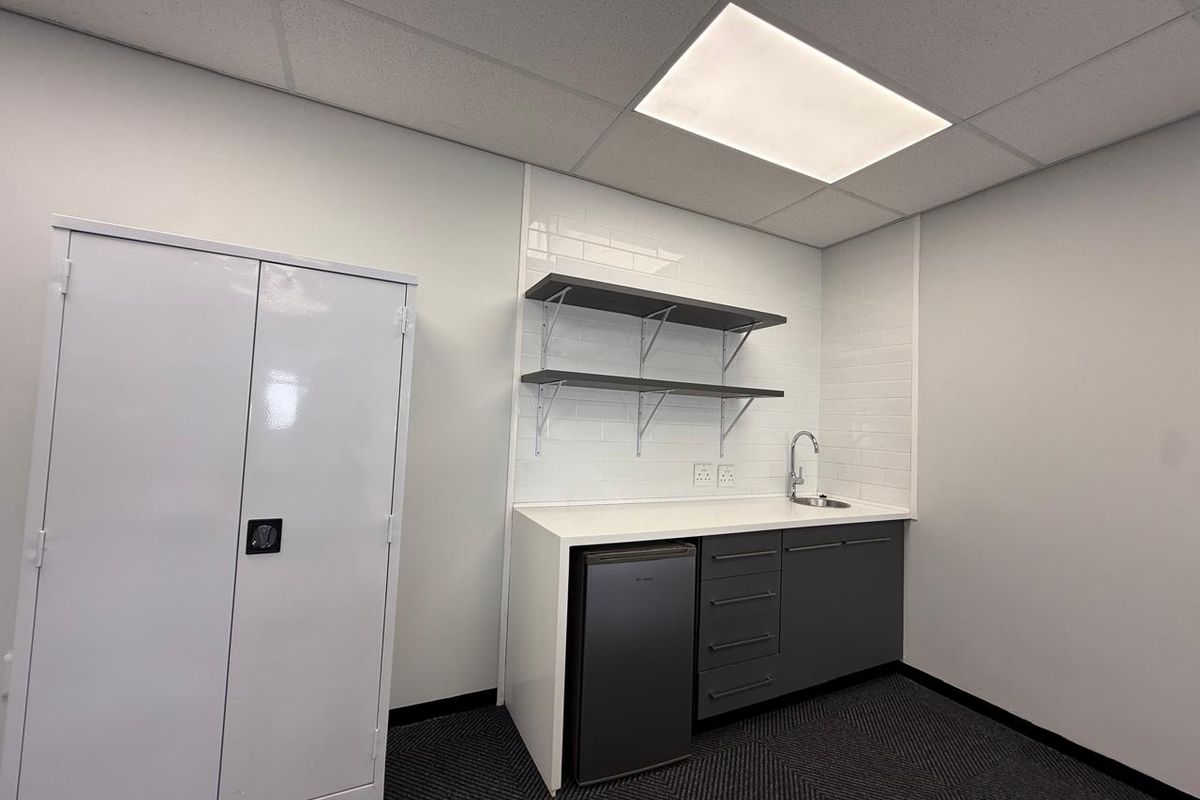 A clean office kitchenette featuring a sink, built-in cabinetry, open shelving, and a tiled backsplash, providing a functional break area for staff.