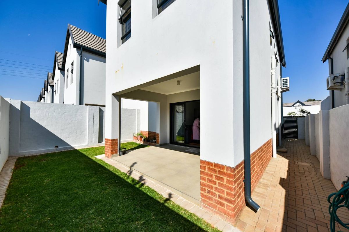 Rear view of the townhouse featuring a covered patio, paved walkway, and a private garden area with boundary walls.