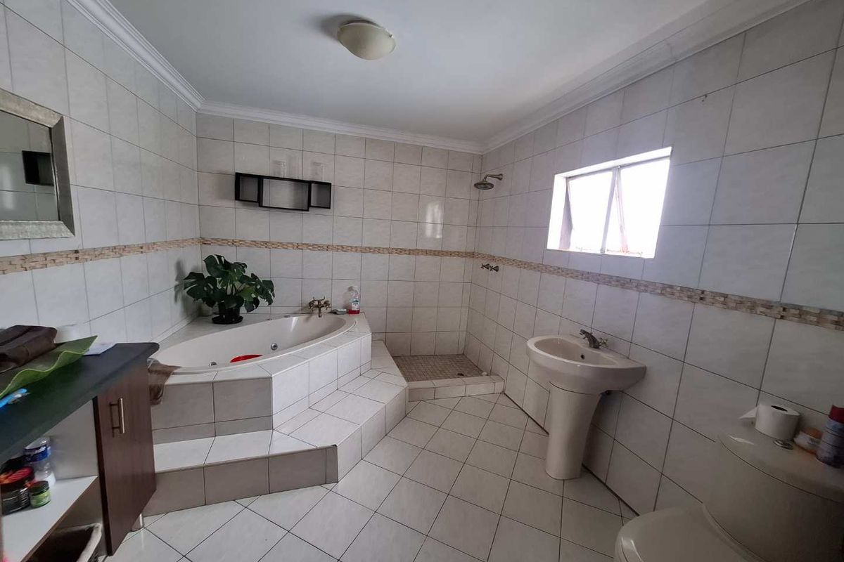 A spacious bathroom featuring a corner bathtub, a walk-in shower, a pedestal basin, and a toilet, finished with neutral wall and floor tiling.