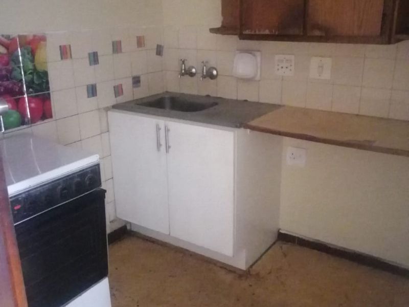 A compact kitchen area featuring built-in cabinetry, a stainless steel sink, and a stove, requiring cosmetic updates and flooring repairs.