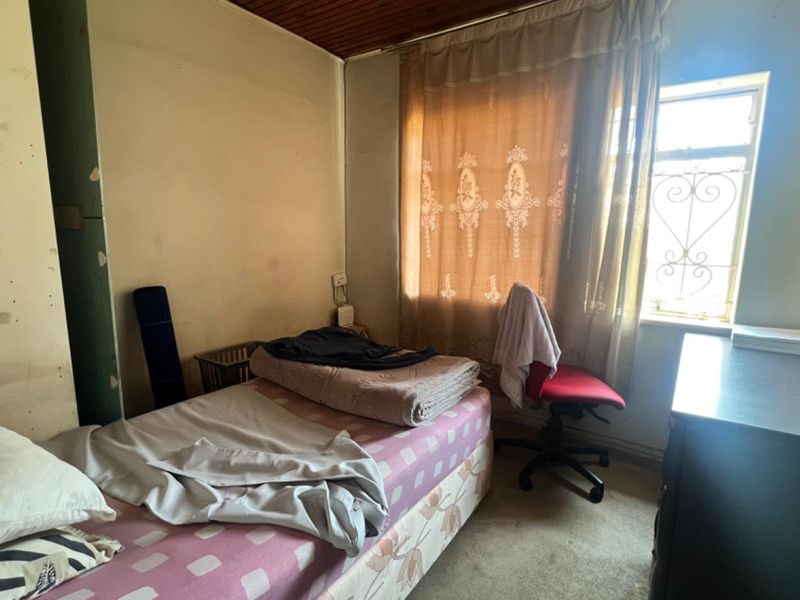 A bedroom featuring a timber ceiling and a window with a security gate, requiring cosmetic updates and wall repairs to improve its overall condition.