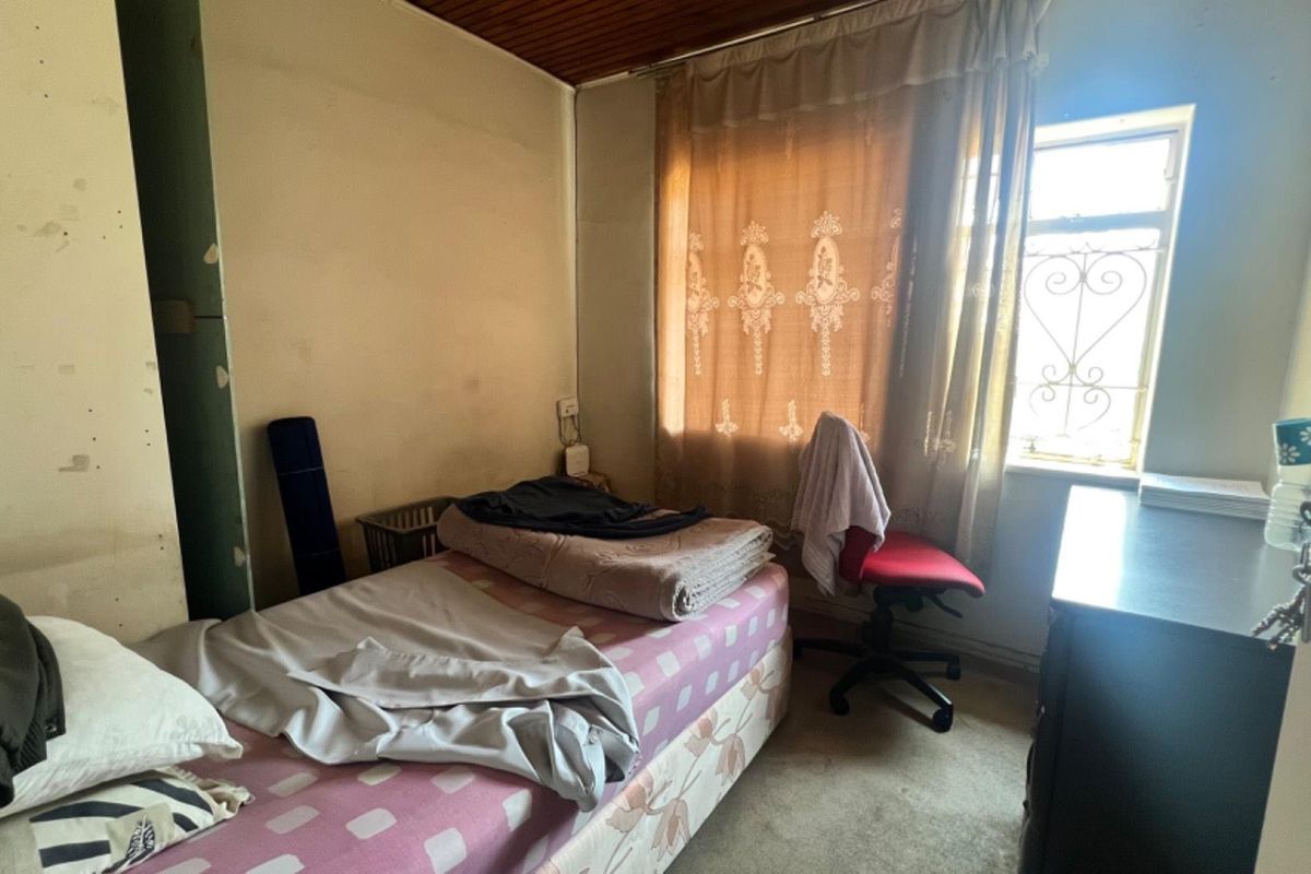 A bedroom featuring a timber ceiling and a window with a security gate, requiring cosmetic updates and wall repairs to improve its overall condition.