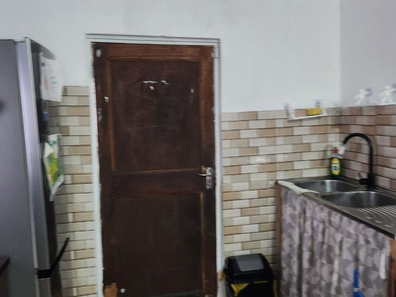 A functional kitchen area featuring a double sink, tiled backsplash, and tiled flooring, with a wooden door leading to an exterior space.
