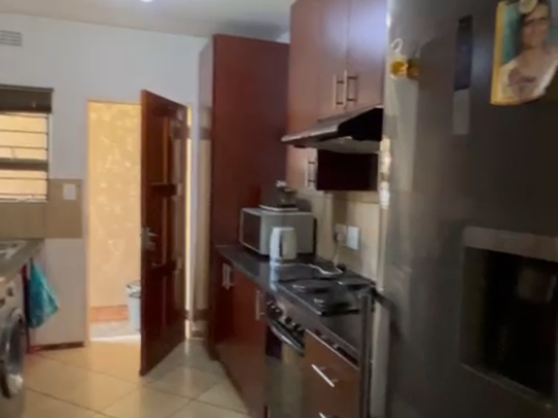 A functional kitchen featuring built-in cabinetry, dark countertops, and integrated appliances with tiled flooring, leading to an adjacent utility area.