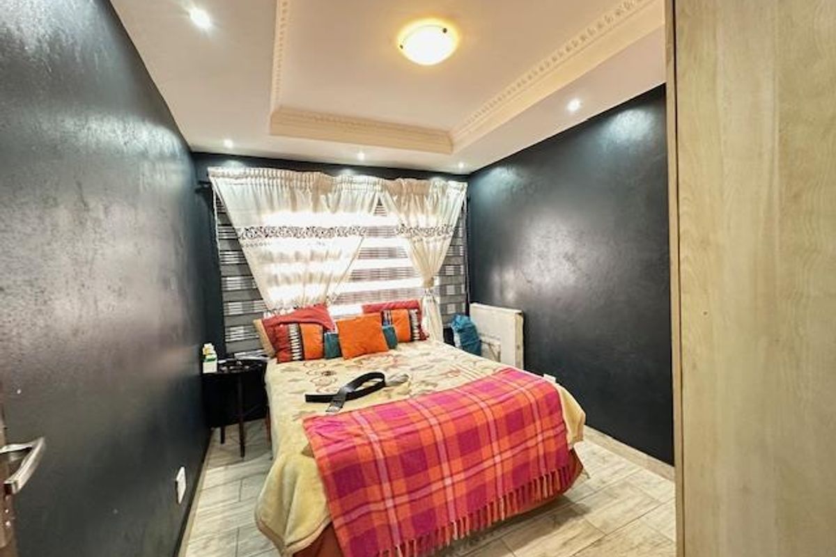 A bedroom featuring dark painted walls, recessed ceiling lighting with decorative molding, and light-toned tiled flooring.