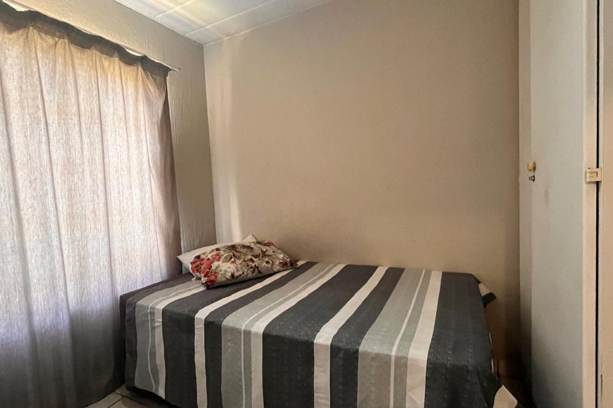 A functional bedroom featuring built-in cupboard storage and natural light through a window with curtaining.