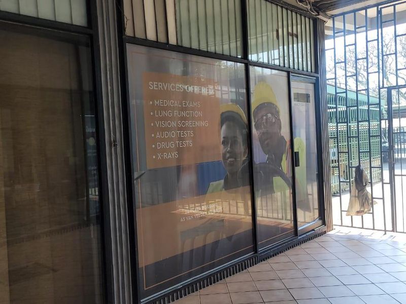Front entrance of a commercial medical facility featuring large glass storefront windows, metal security gates, and tiled flooring.