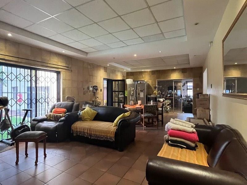 Spacious open-plan living area featuring tiled floors, stone wall accents, and a suspended ceiling with recessed lighting, leading out to a patio.