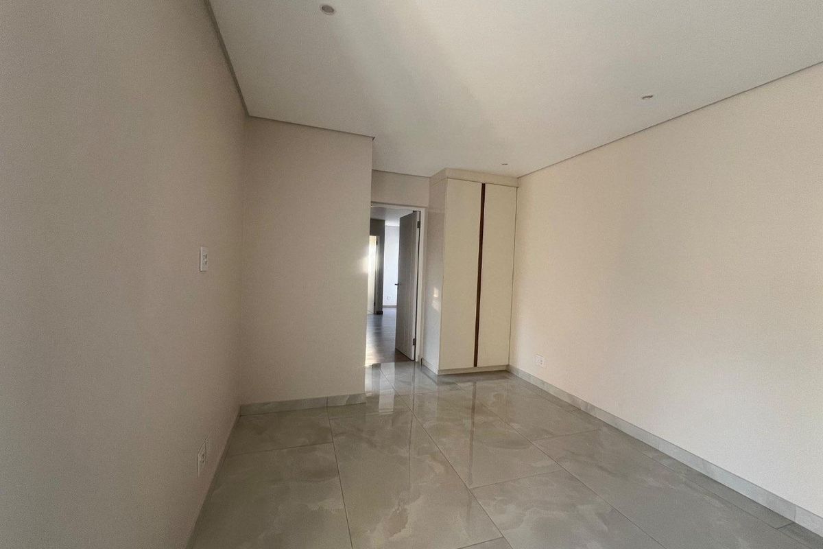 A bright, empty bedroom featuring neutral walls, polished porcelain floor tiles, and a built-in wardrobe with clean, modern lines.