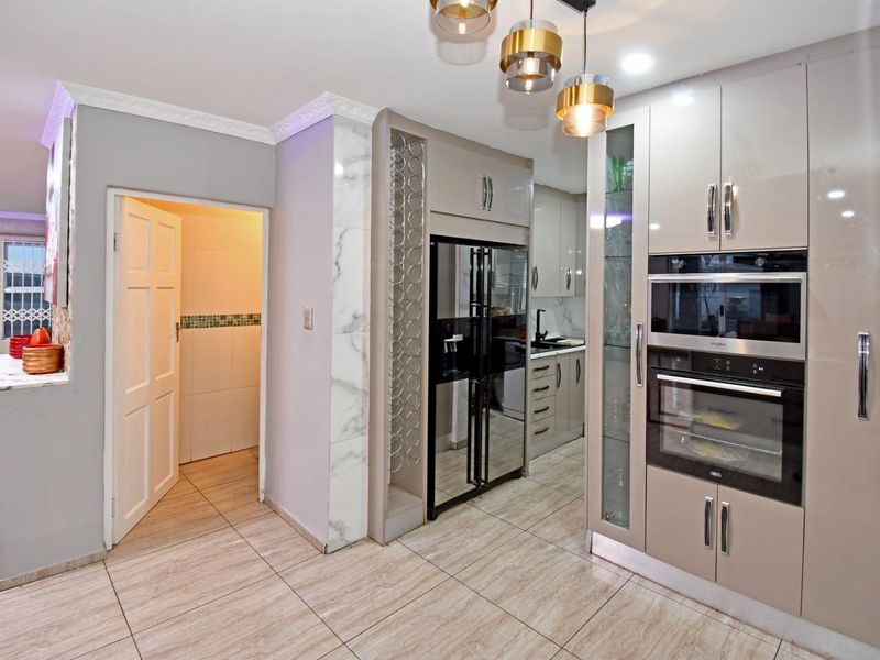 Modern kitchen featuring high-gloss cabinetry, integrated oven and microwave, wine storage, and elegant tiled flooring with contemporary pendant lighting.