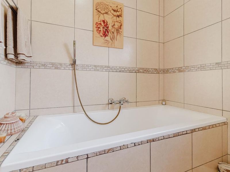 A clean bathroom featuring a built-in bathtub with a wall-mounted shower mixer, finished with neutral ceramic wall tiles and a decorative mosaic border.