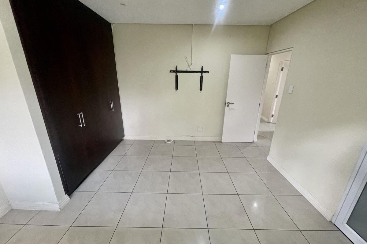 An empty bedroom featuring neutral tiled flooring and dark wood built-in cupboards, providing a clean and versatile space.