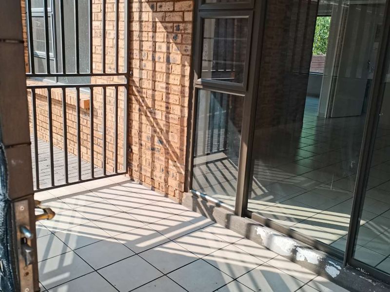 A tiled balcony area featuring exposed brick walls, security gate, and sliding glass doors leading into the apartment interior.