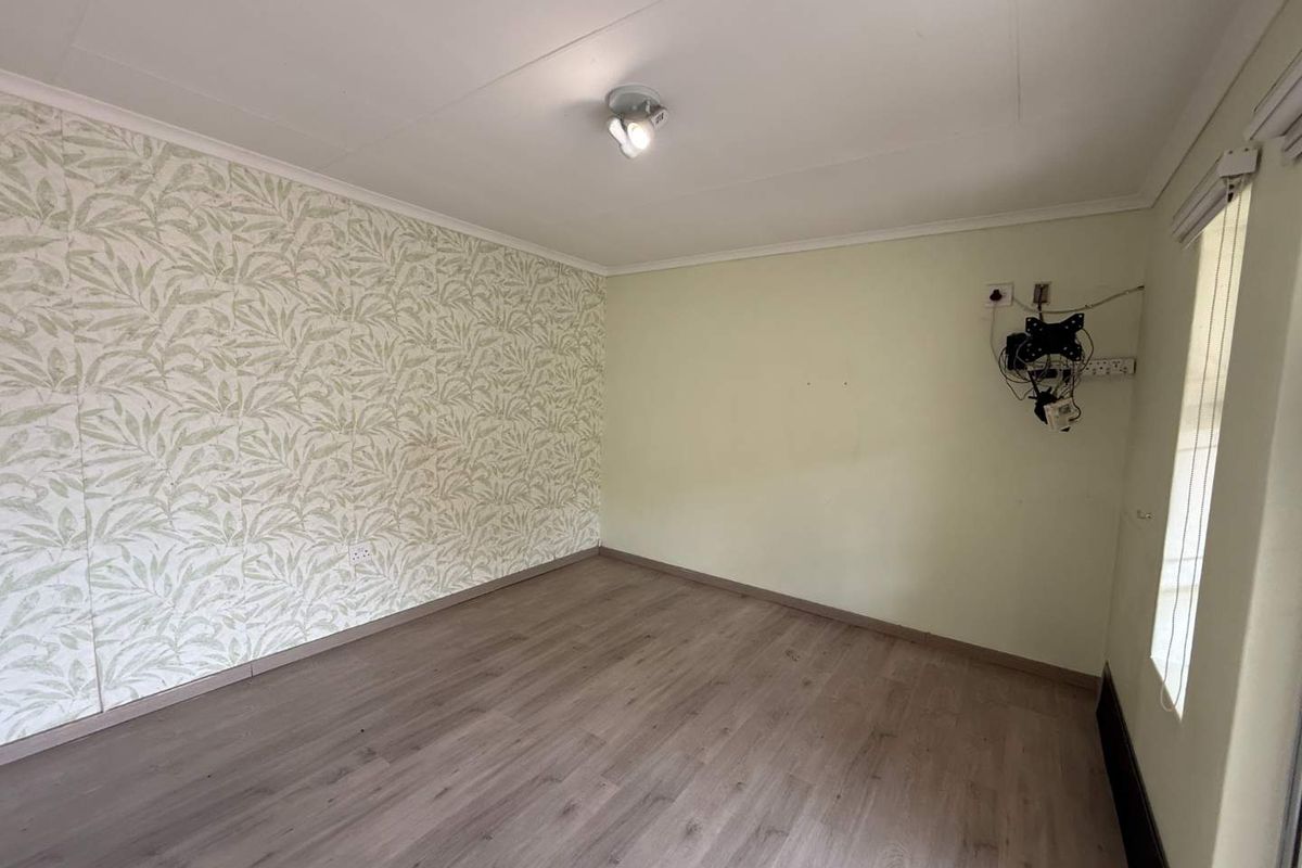A vacant bedroom featuring wood-look laminate flooring, a patterned feature wall, and a ceiling-mounted light fixture.