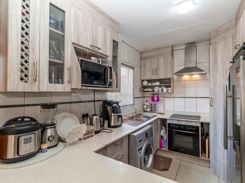 A functional kitchen featuring light wood-grain cabinetry, stone-look countertops, integrated appliances including an oven and extractor fan, and tiled finishes.