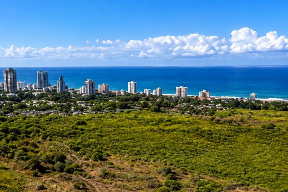 An elevated aerial view showcasing the coastal landscape, surrounding greenery, and distant city skyline along the oceanfront.
