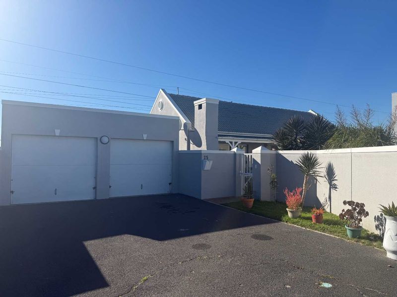 Front elevation of the property featuring a double garage, paved driveway, and secure boundary wall with pedestrian access.