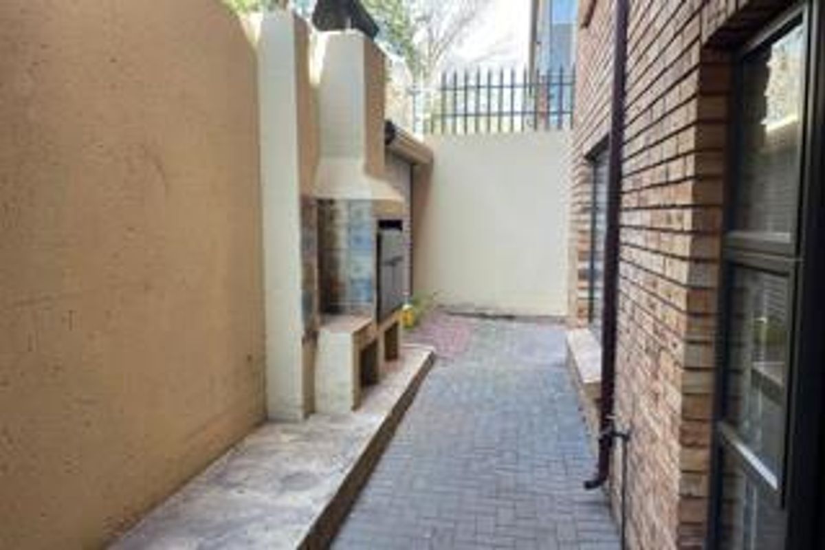 A narrow rear courtyard featuring a built-in braai, paved flooring, and high boundary walls with security fencing.