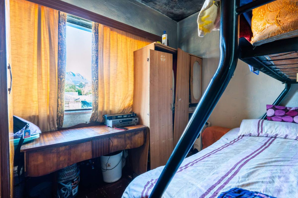 A bedroom featuring a built-in wooden desk and wardrobe, with significant ceiling and wall damage requiring maintenance and refurbishment.