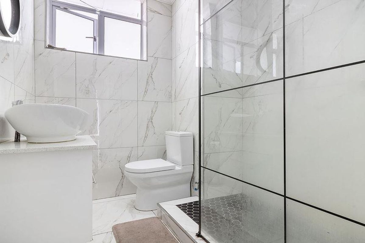 Modern bathroom featuring marble-look wall and floor tiles, a glass-enclosed shower, a contemporary vessel sink vanity, and a white toilet.