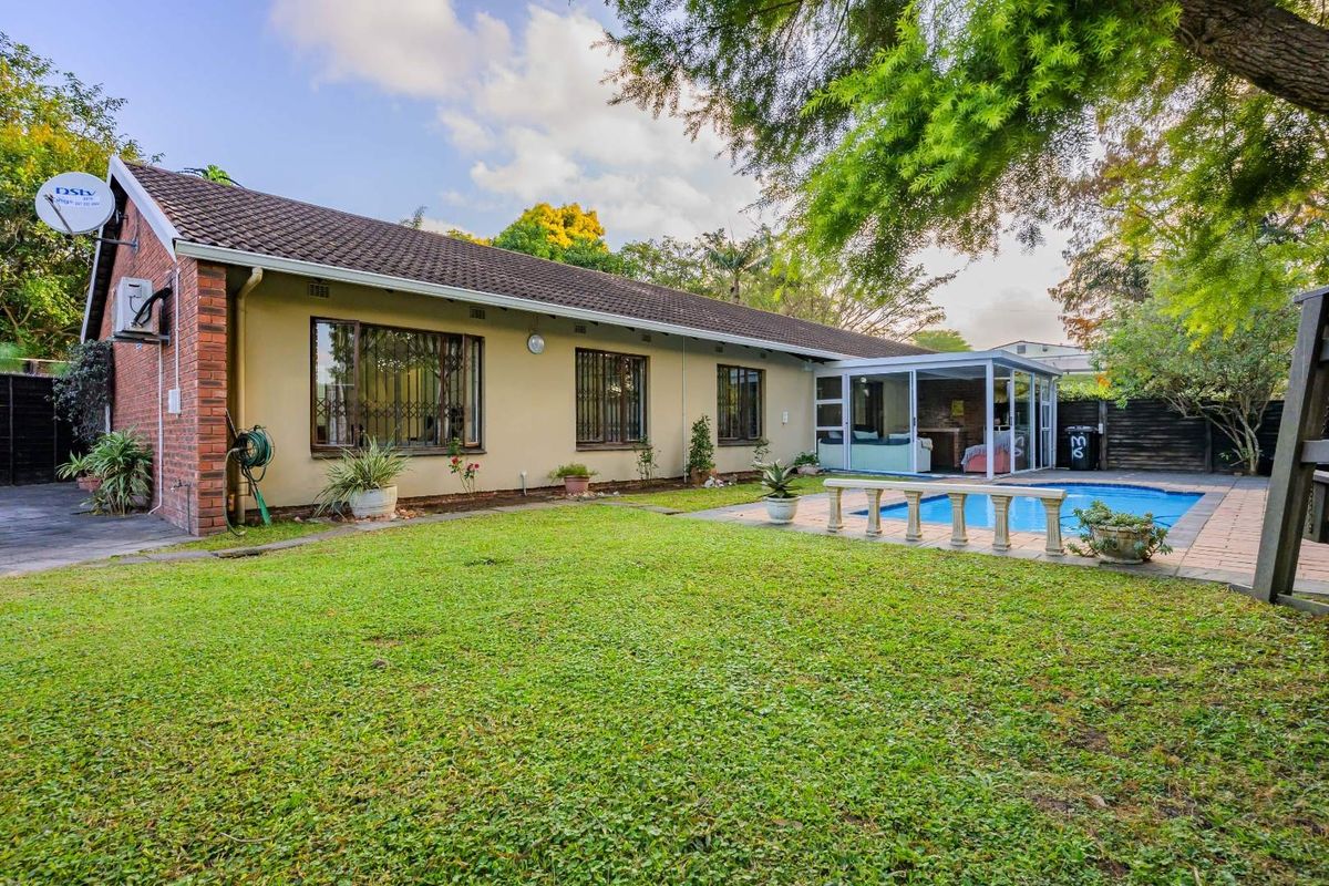 Rear view of the townhouse featuring a landscaped garden, a swimming pool, and an enclosed patio area with brick and tile construction.