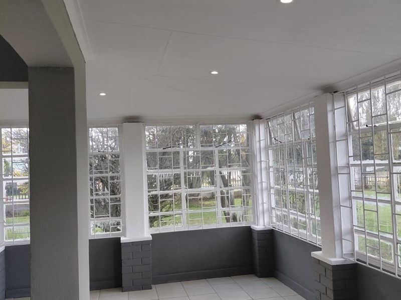 A bright, enclosed patio area featuring tiled flooring, recessed lighting, and large windows with security bars, offering a clear view of the garden.
