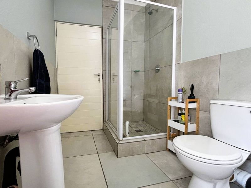 A clean, modern bathroom featuring a pedestal basin, a glass-enclosed shower, and neutral ceramic tiling throughout.