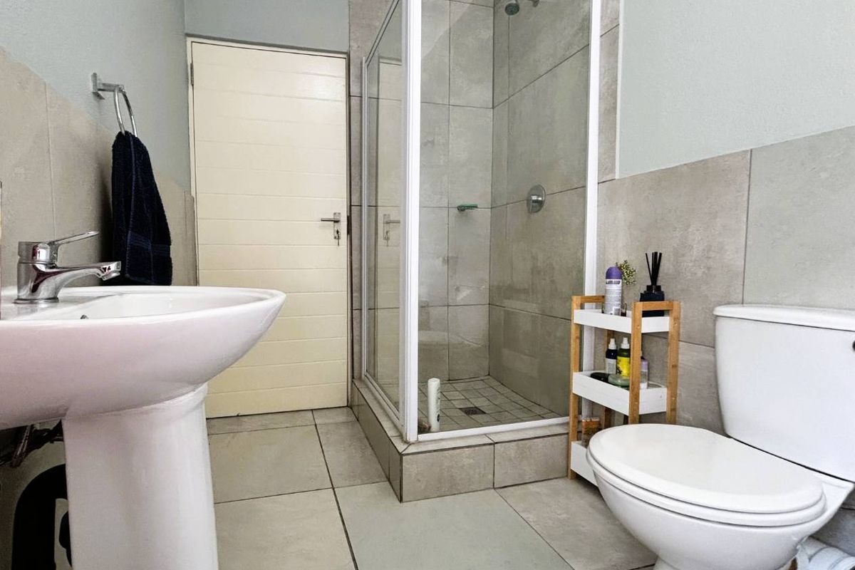 A clean, modern bathroom featuring a pedestal basin, a glass-enclosed shower, and neutral ceramic tiling throughout.