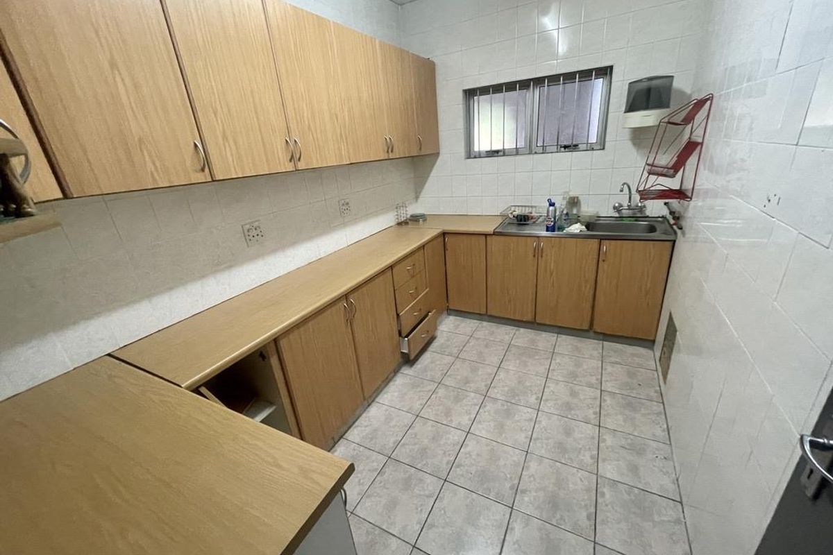 A functional office kitchenette featuring light wood-finish cabinetry, tiled walls, and a stainless steel sink with tiled flooring.