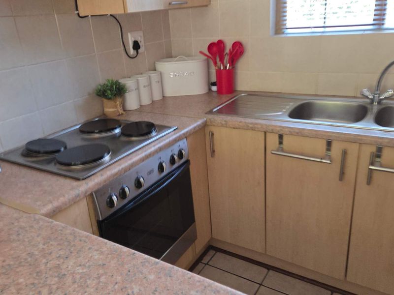 A functional kitchen featuring laminate countertops, a stainless steel sink, built-in cabinetry, and an integrated electric hob and oven with tiled backsplash.
