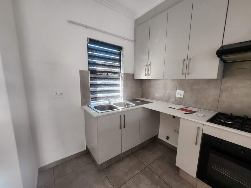 Modern kitchen featuring sleek built-in cabinetry, a double sink, gas hob, integrated oven, extractor fan, and neutral tiled finishes.