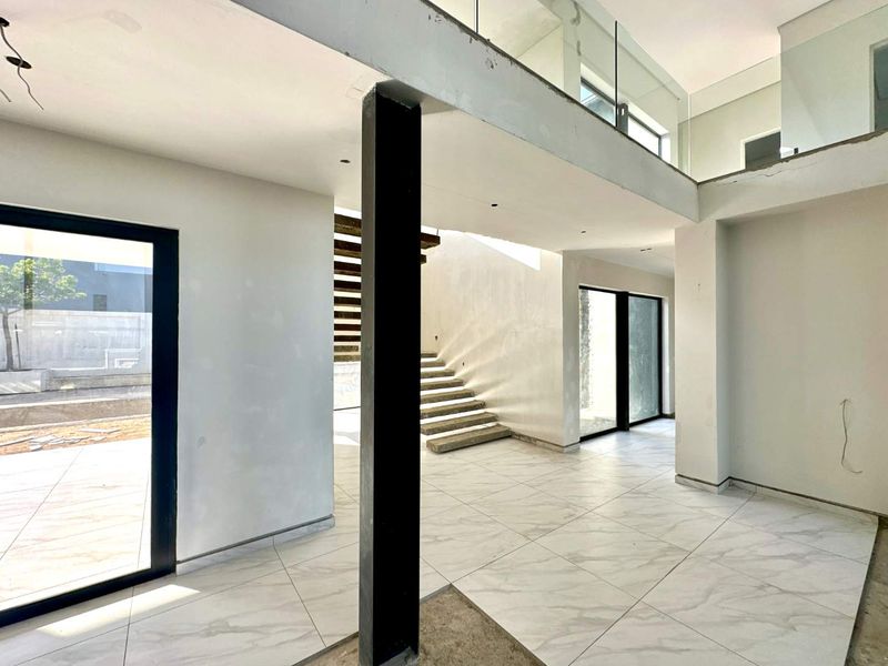 Spacious open-plan living area under construction, featuring a modern staircase, mezzanine level with glass balustrade, and large sliding doors leading to the exterior.